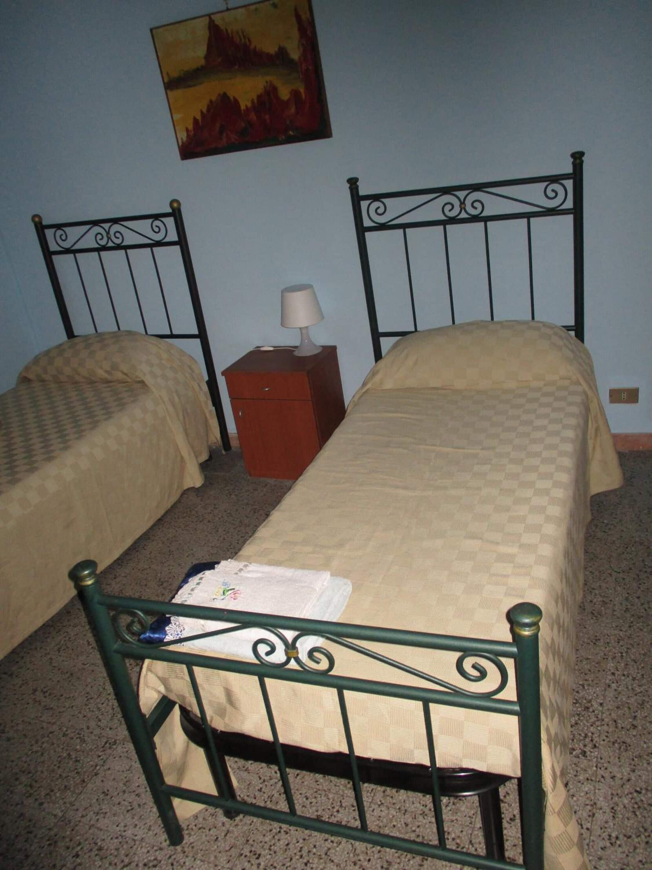 A room with two single beds, a nightstand with a lamp, and a painting on the wall.