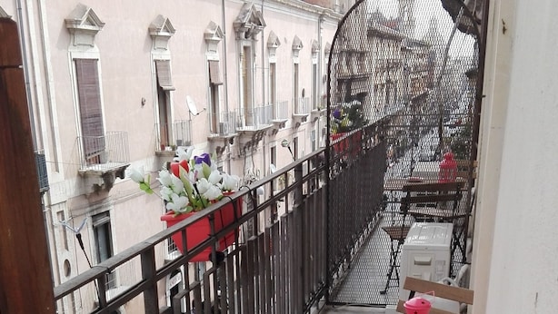 Un balcón con una banca de madera, una mesita con un farolillo rosa y una valla de metal.