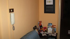 Habitación de hotel con teléfono integrado en la pared, un calendario y una mesa con folletos varios y un altavoz pequeño.