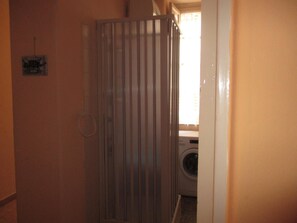 A narrow hallway with a metal gate, a washing machine, and a small window with curtains.