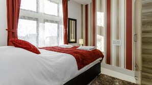 A bedroom with a large bed, red curtains, and striped walls. - City Gate Serviced Apartments (London)