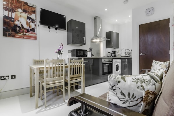 A modern kitchen with a dining area, a sofa, and a TV mounted on the wall.