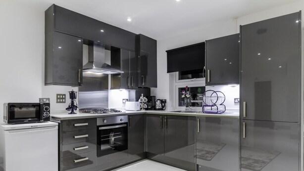 A modern kitchen with dark cabinetry, a microwave, an oven, and a refrigerator. - City Gate Serviced Apartments (London)
