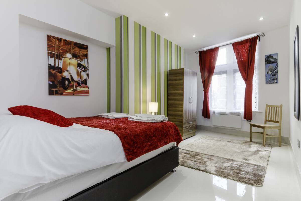 A modern bedroom with a bed, a nightstand, a lamp, a chair, and a window with curtains.