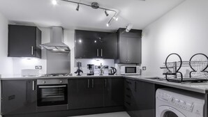 A modern kitchen with dark cabinets, a built-in oven, a microwave, and a washing machine. - City Gate Serviced Apartments (London)