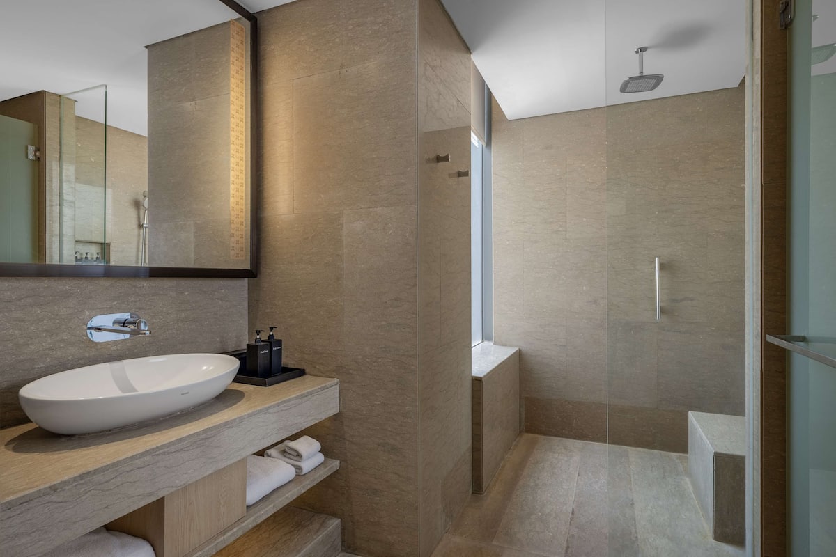 A modern bathroom with a large white sink, a mirror, and a walk-in shower.