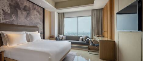 Una habitación de hotel moderna con una cama grande, un sofá, un televisor y vistas a la ciudad.