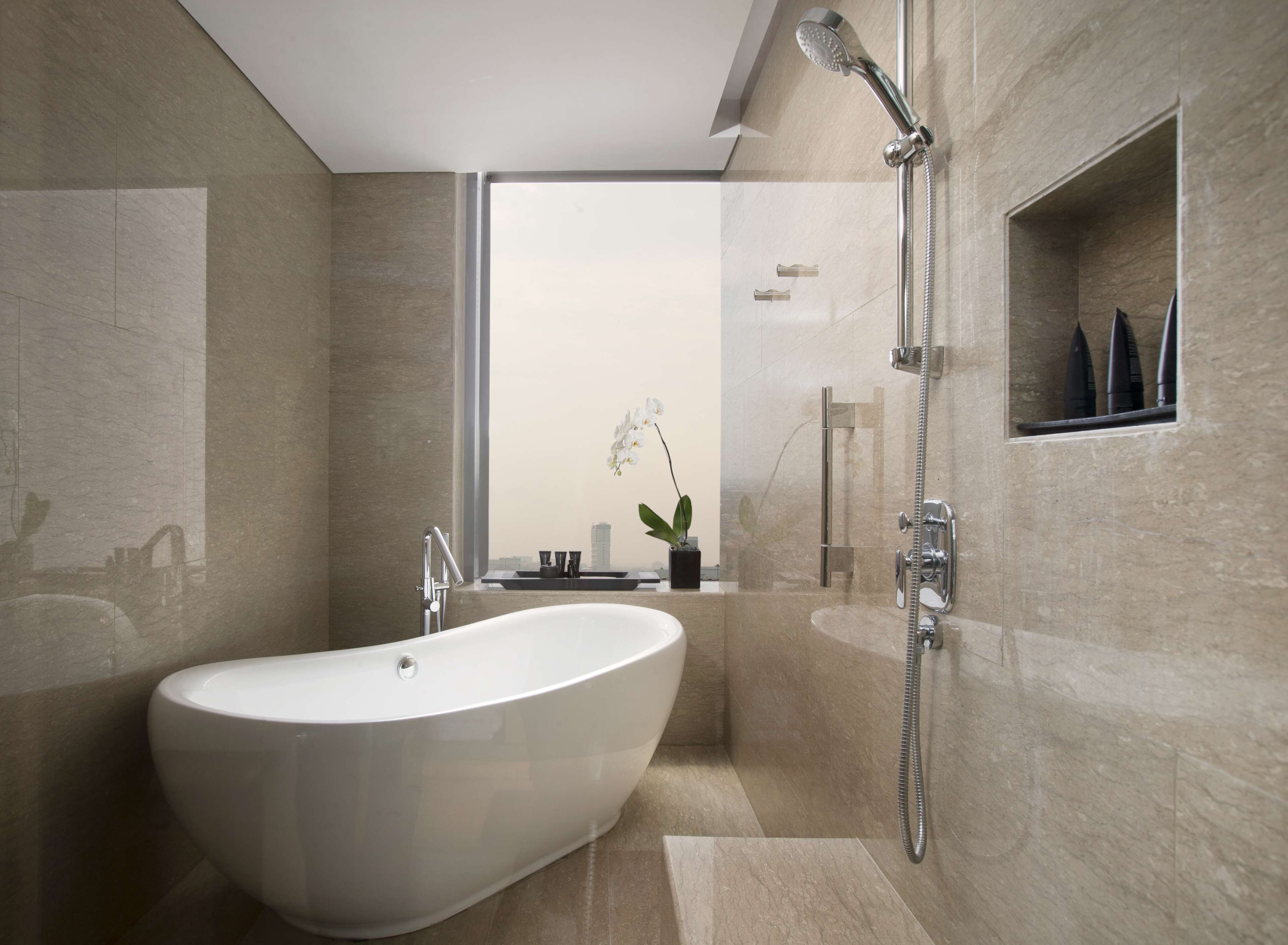 A modern bathroom with a freestanding bathtub, a handheld showerhead, and a small shelf with toiletries.