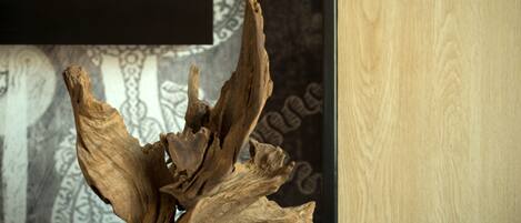 A wooden sculpture with a rough texture and natural curves, placed against a patterned wall with a black shelf above it.