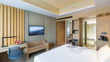 A modern hotel room with a large bed, a desk with a chair, a television, and a bathroom visible through an open door.