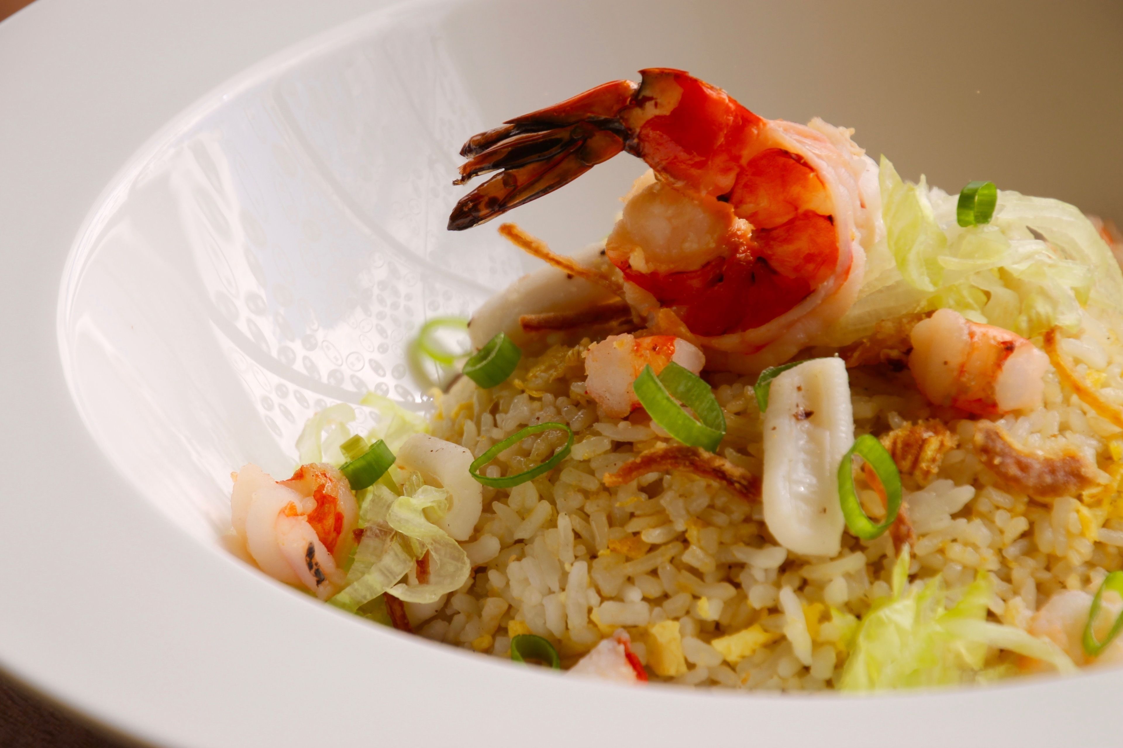 Un tazón de arroz frito con camarones y cebollas verdes.