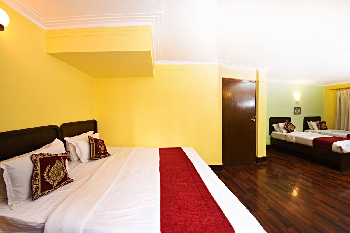 A hotel room with a large bed, a smaller bed, wooden flooring, and a door leading to another room.