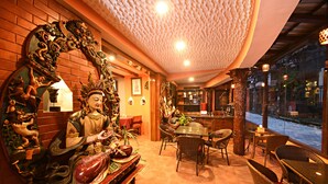 Um interior tradicional com uma estátua de Buda, decorações elaboradas e uma área de jantar com mobiliário de vime.