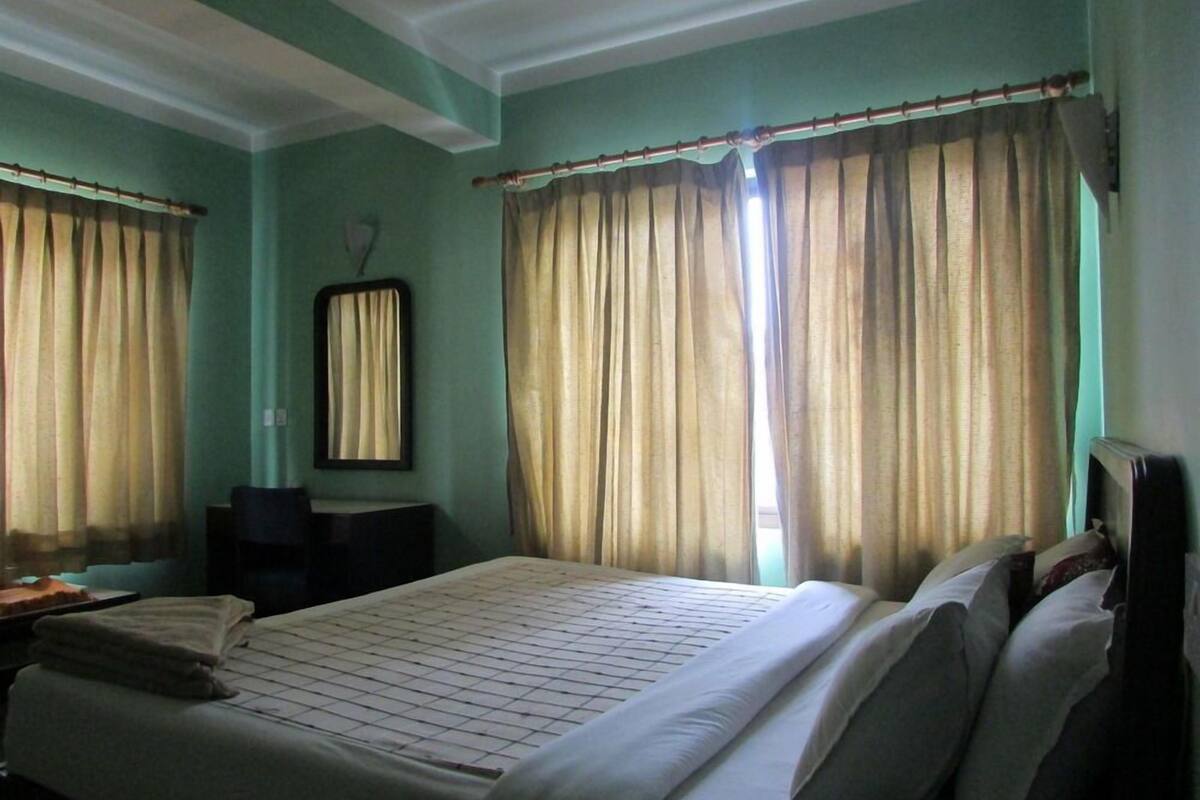 A hotel room with a bed, curtains, a chair, and a desk.