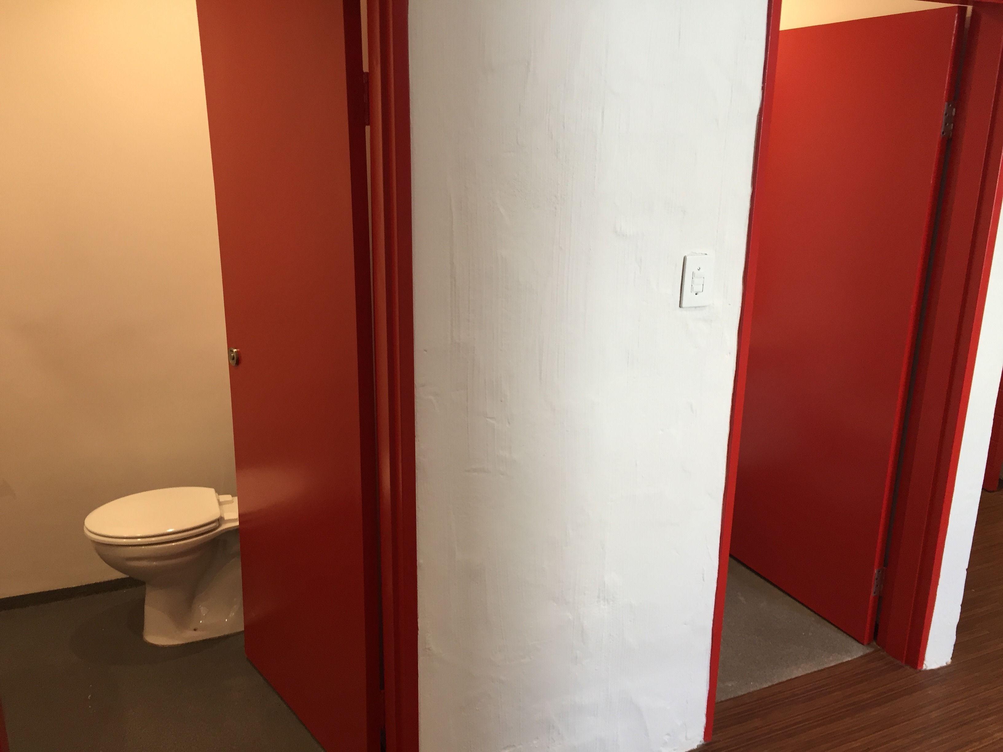 Un baño con un inodoro blanco, puertas rojas y una pared blanca.