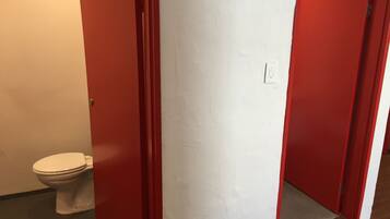 Un baño con un inodoro blanco, puertas rojas y una pared blanca.