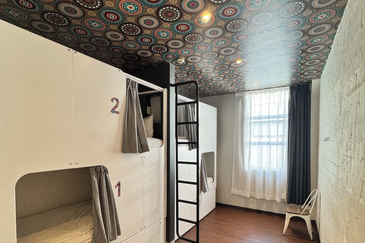 Un dormitorio con literas, una escalera, una ventana con cortinas y un techo estampado.