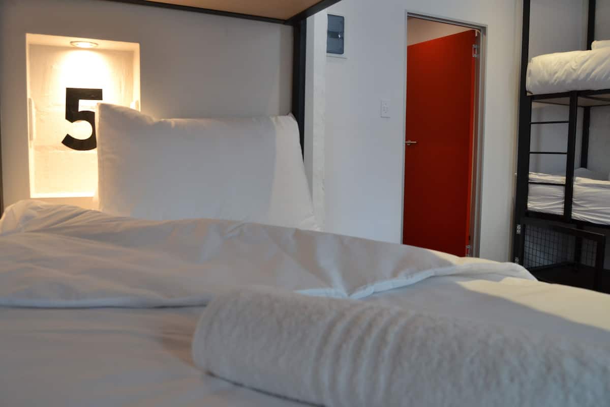 Habitación de hotel con cama, puerta roja y literas en una esquina.