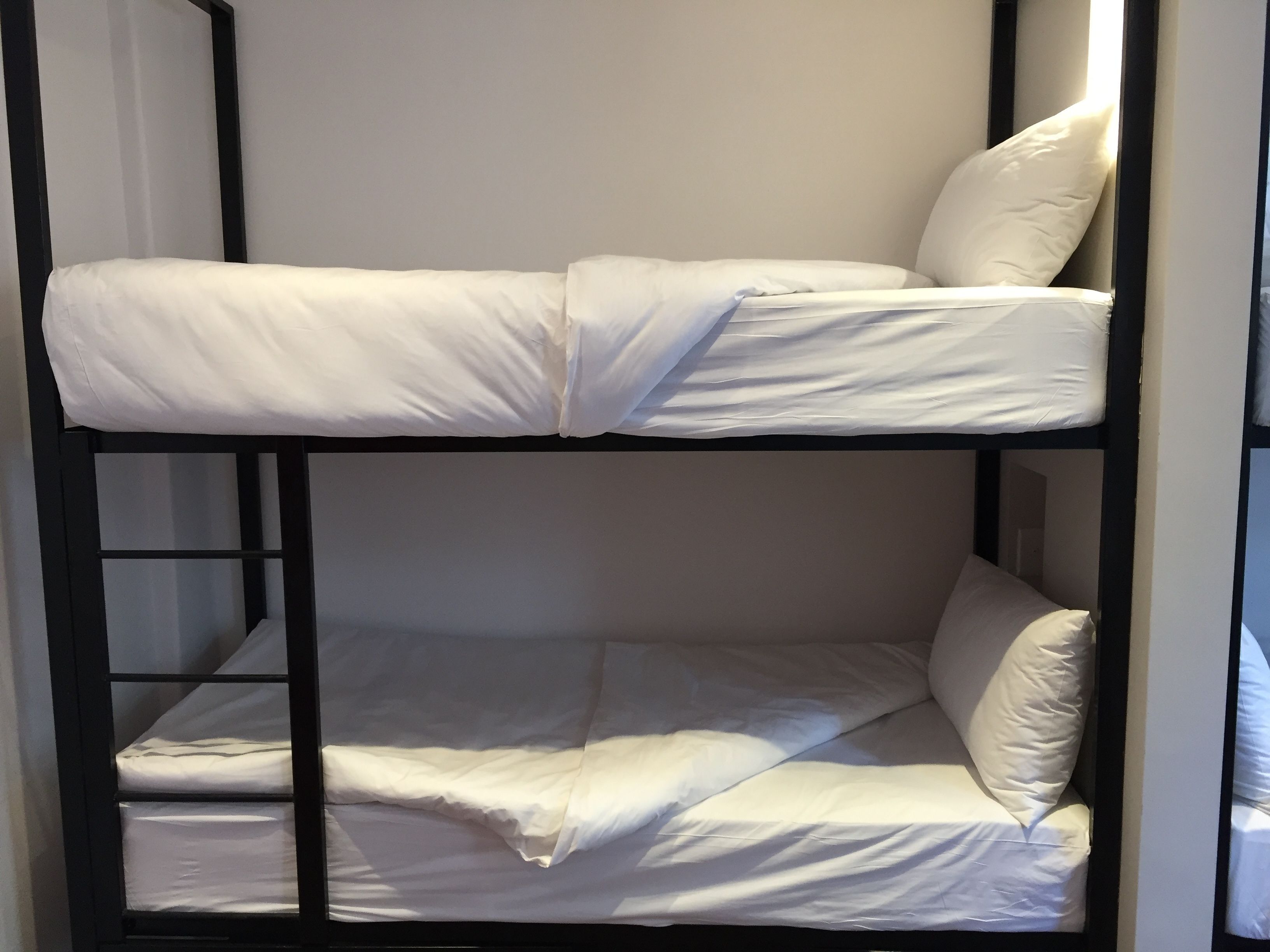A bunk bed with white bedding and black metal frame.