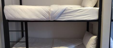 A bunk bed with white bedding and black metal frame.