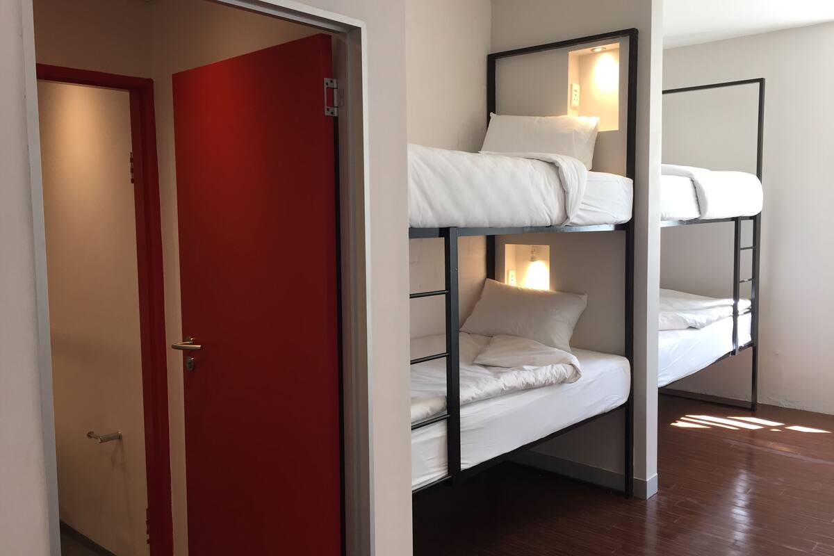 Una cama litera de dos niveles, una puerta roja y un pasillo.
