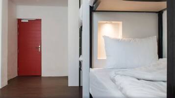 A room with a single bed, a red door, and a small window with a light.