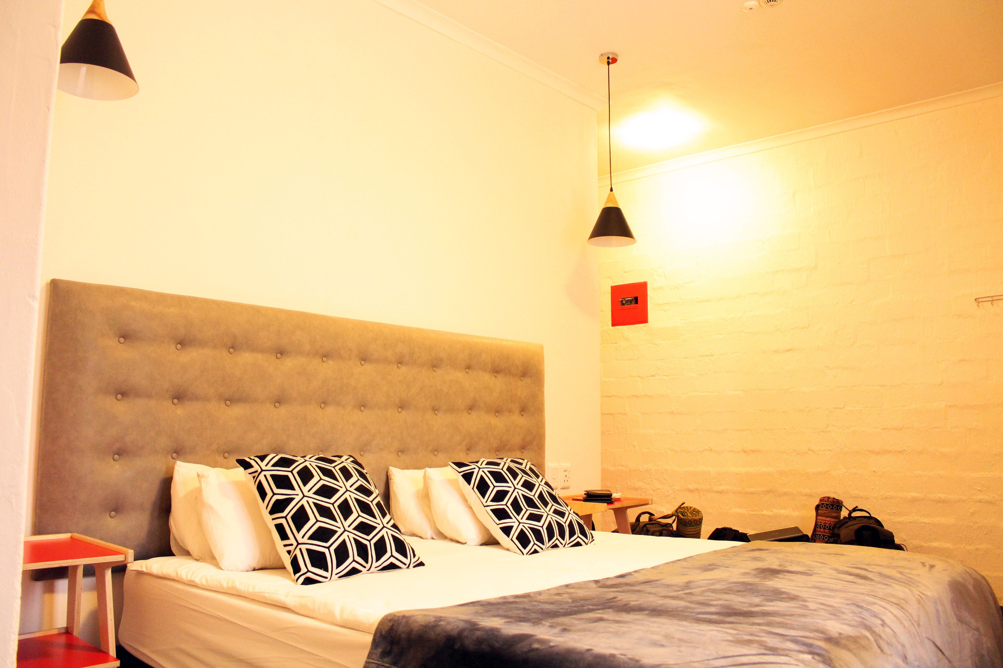 A neatly made bed with a tufted headboard, a bedside table, and a hanging lamp.