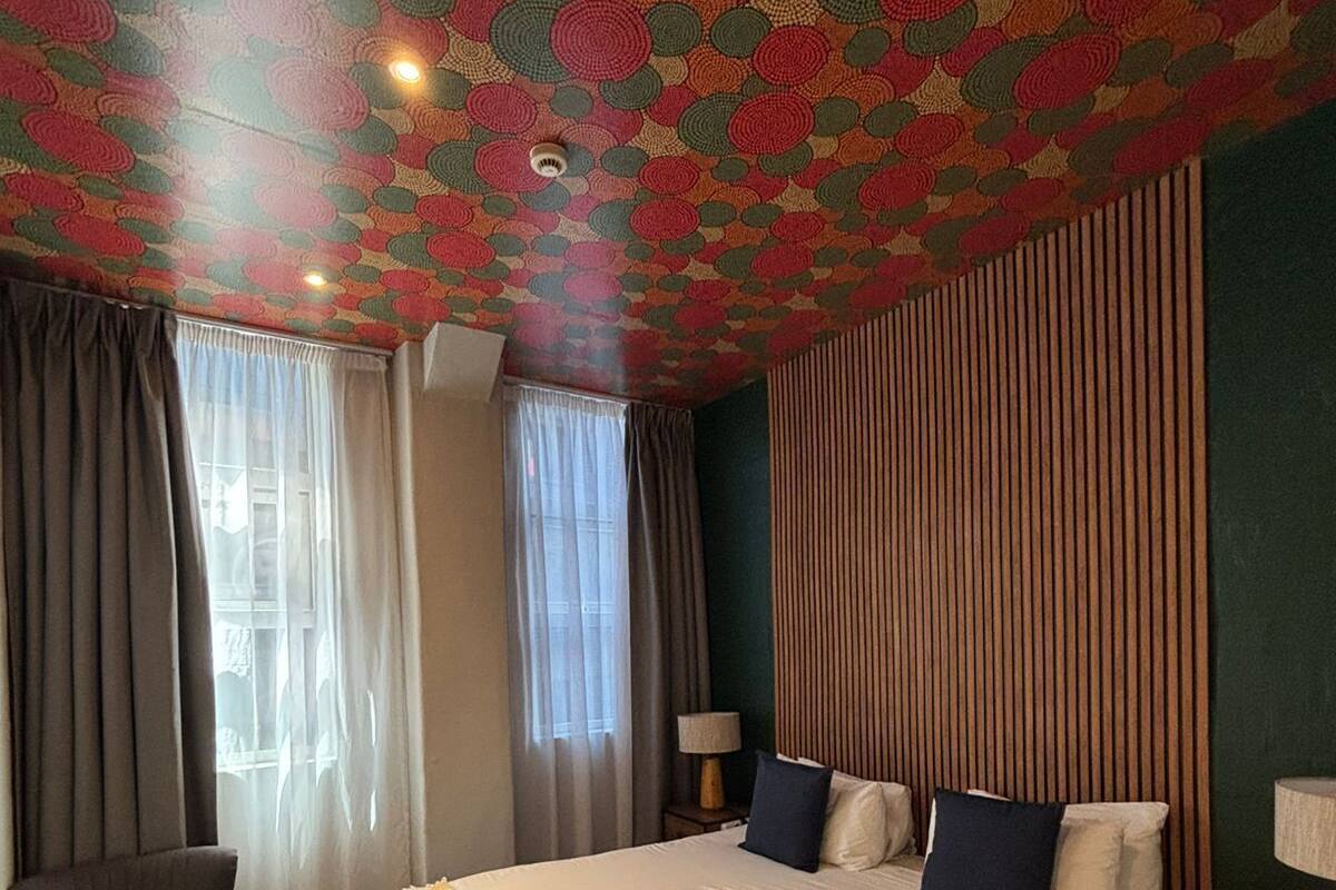 Habitación de hotel con una cama grande, dos mesitas de noche, una silla y un techo con diseño.