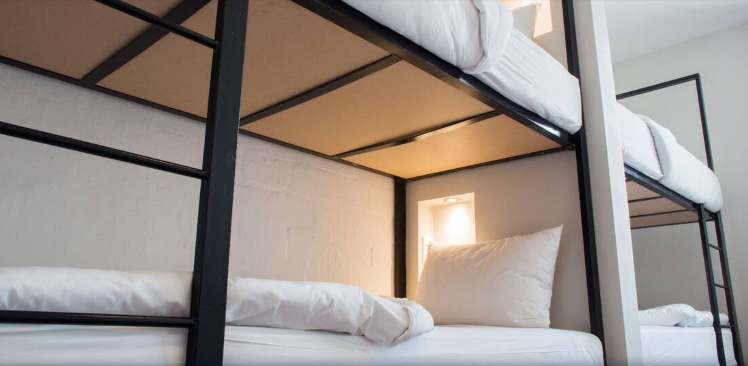 Une chambre avec un lit superposé, dotée de linge de lit blanc et d’une fenêtre laissant entrer la lumière naturelle.