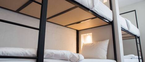 Une chambre avec un lit superposé, dotée de linge de lit blanc et d’une fenêtre laissant entrer la lumière naturelle.