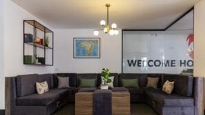 A modern reception area with a sectional sofa, a wooden coffee table, a map on the wall, and a 'WELCOME HOME' sign. - 91 Loop - Hostel (Cape Town)