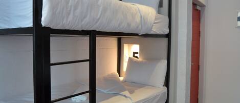 Una cama individual superpuesta con ropa de cama blanca y una ventana pequeña con luz.