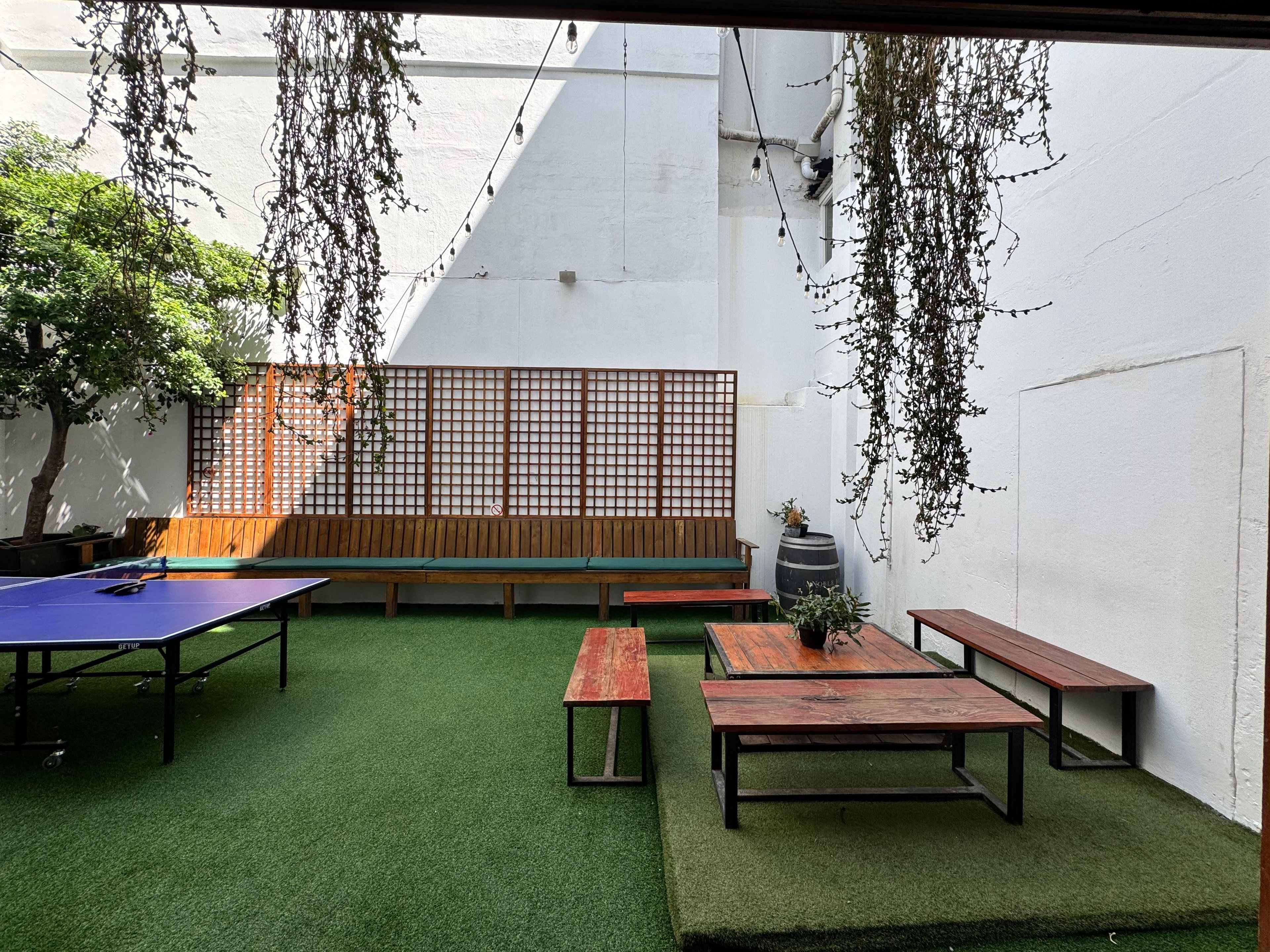 A courtyard with artificial grass, wooden benches, a ping pong table, and hanging plants.