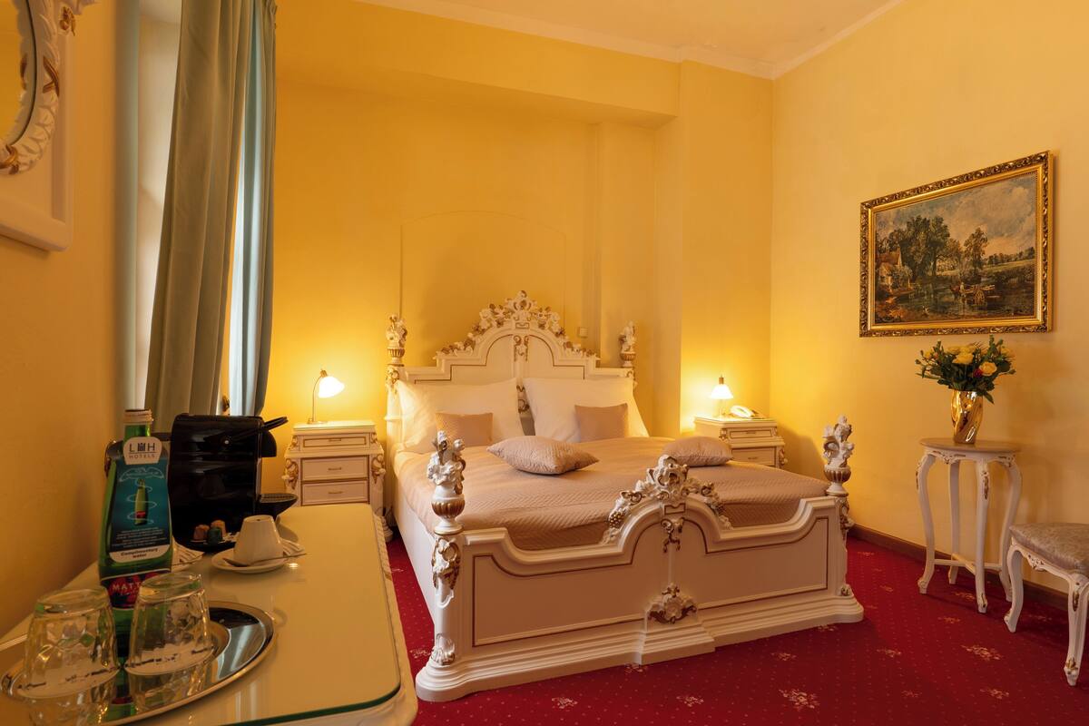 Una habitación de hotel con una cama grande, mesitas de noche, un aparador y un cuadro en la pared.