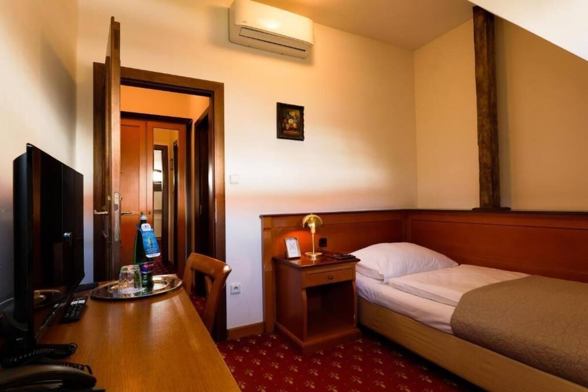 Una habitación de hotel con cama, mesita de noche, lámpara, televisor y escritorio con silla.