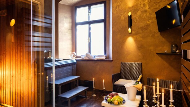 Een moderne spa-ruimte met een houten bank, een tafel met fruit en een champagnefles, en een groot raam met uitzicht.
