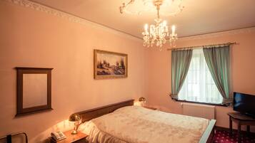 Una habitación de hotel con una cama, un escritorio con lámpara, televisión, ventana con cortinas y un cuadro en la pared.