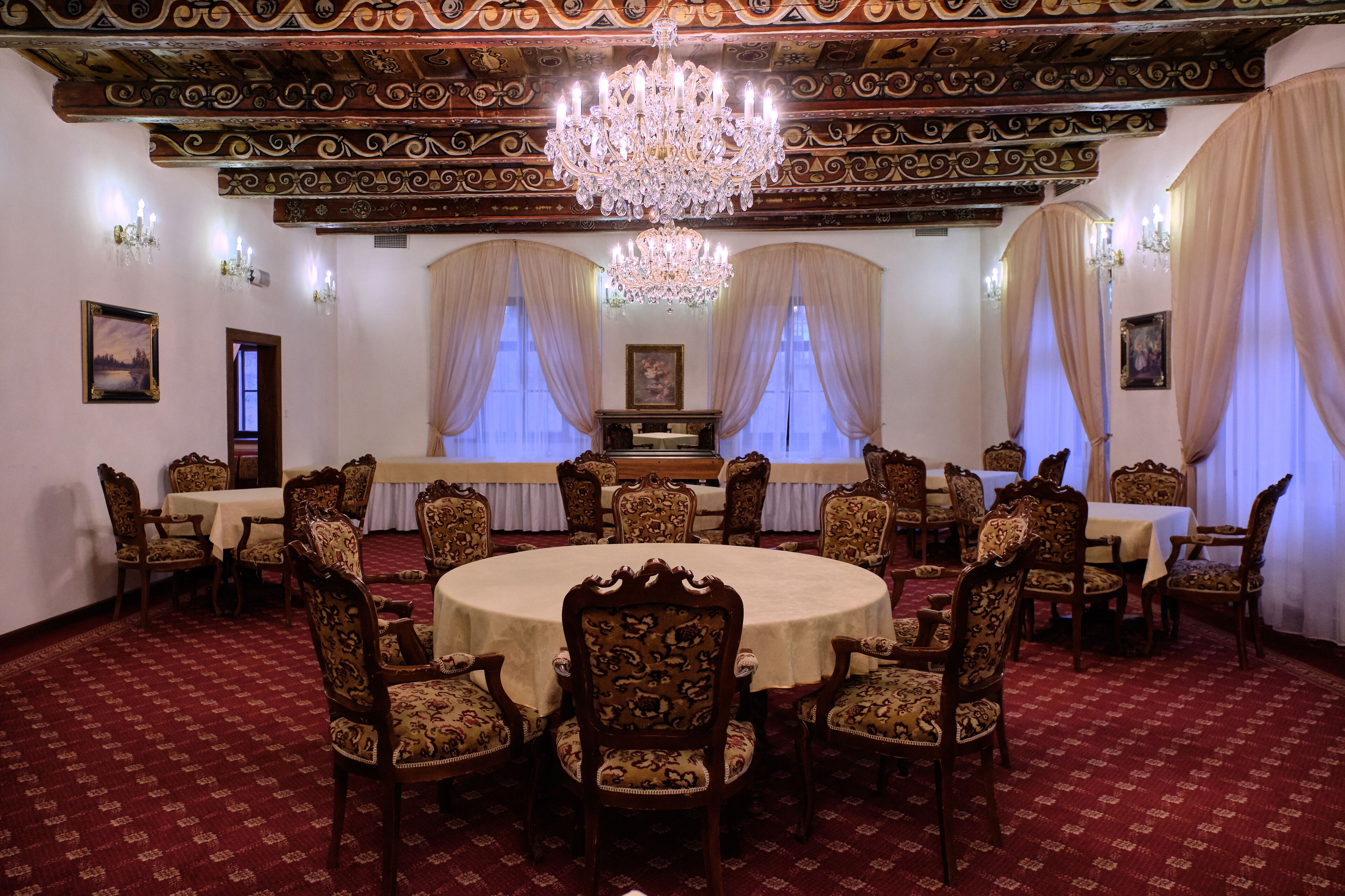 Ein formeller Speisesaal mit aufwendigen Kronleuchtern, runden Tischen und klassischen Holzstühlen.