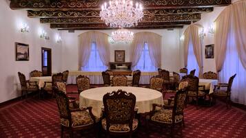 Ein formeller Speisesaal mit aufwendigen Kronleuchtern, runden Tischen und klassischen Holzstühlen.