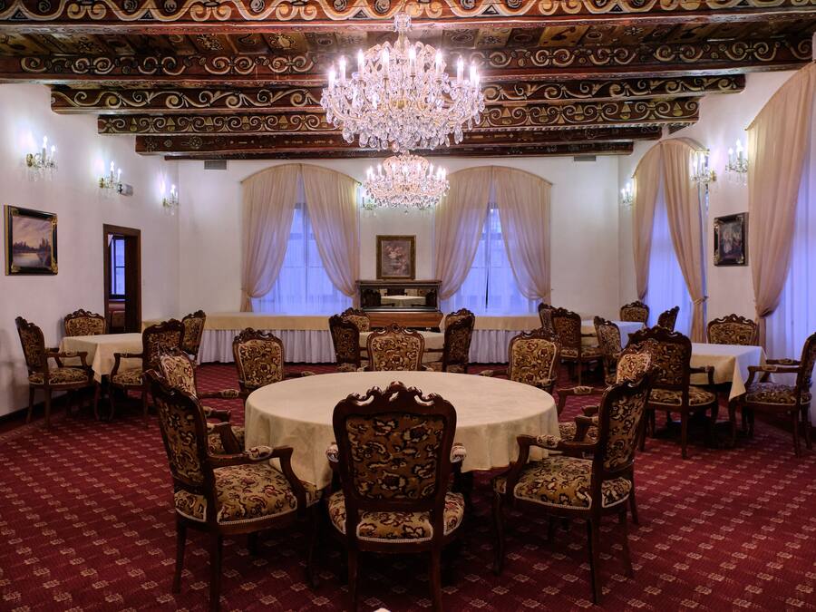 A formal dining room with ornate chandeliers, round tables, and classic wooden chairs.