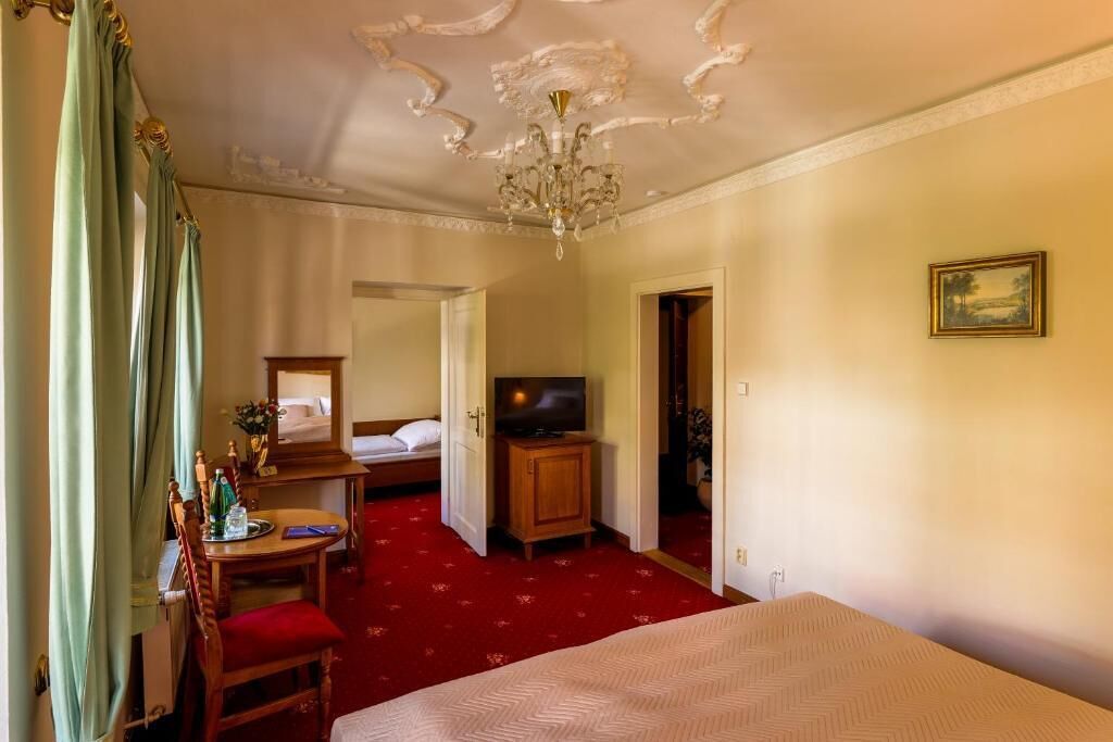 Une chambre d’hôtel avec un lit, une télévision, un bureau avec une chaise et un sol recouvert d’une moquette rouge.