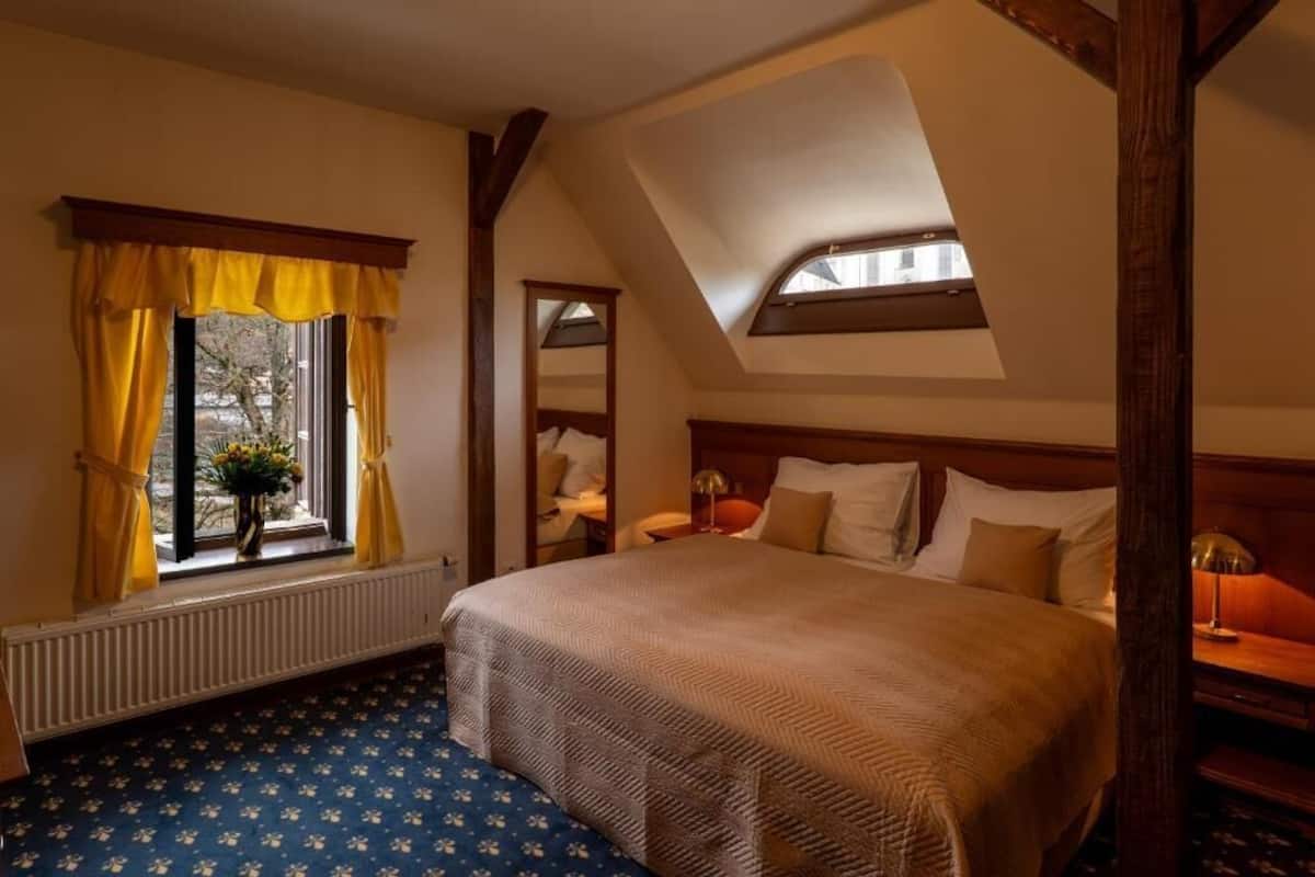 Un dormitorio con una cama grande, una ventana con cortinas amarillas, un tragaluz y un radiador.