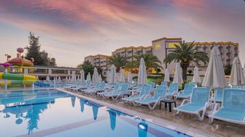 Relax by the pool surrounded by palm trees and shaded by umbrellas.