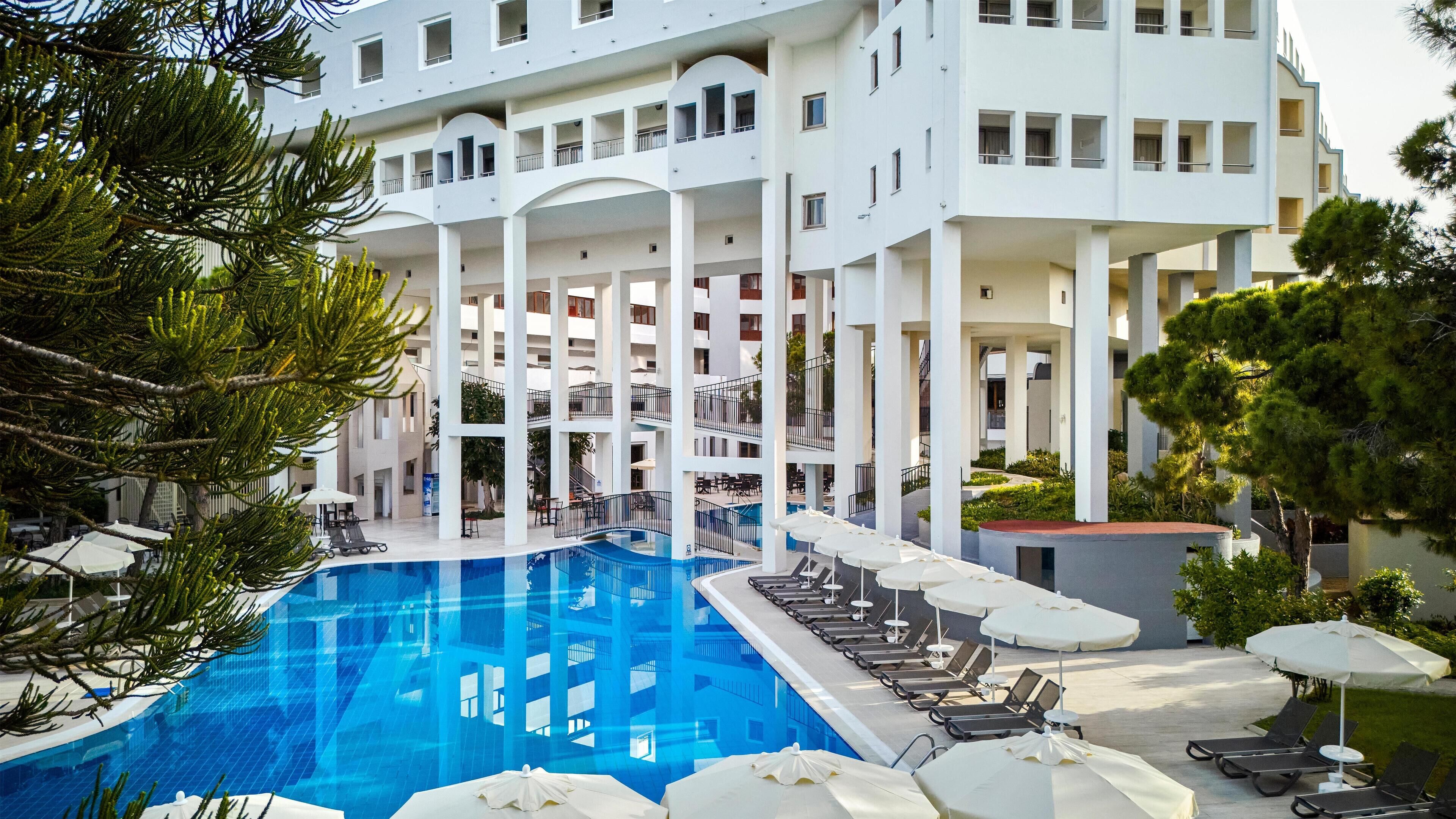A modern hotel with a central swimming pool, multiple balconies, and outdoor seating areas.