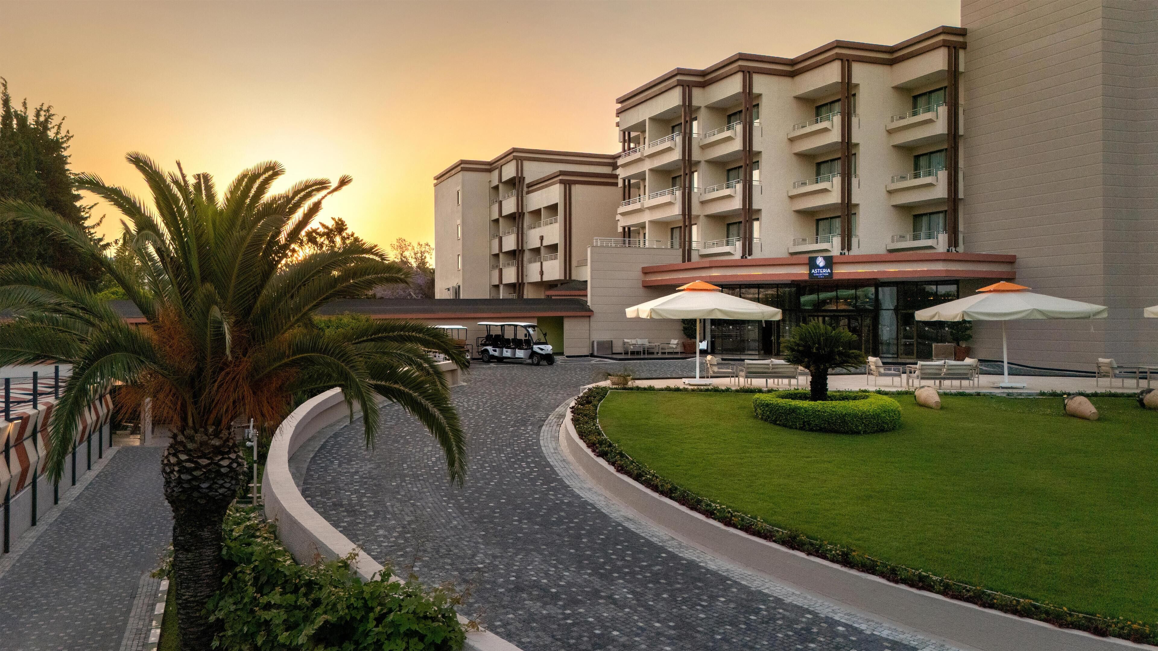 Un hotel moderno con un camino curvo, mobiliario exterior con sombrillas y un carrito de golf.