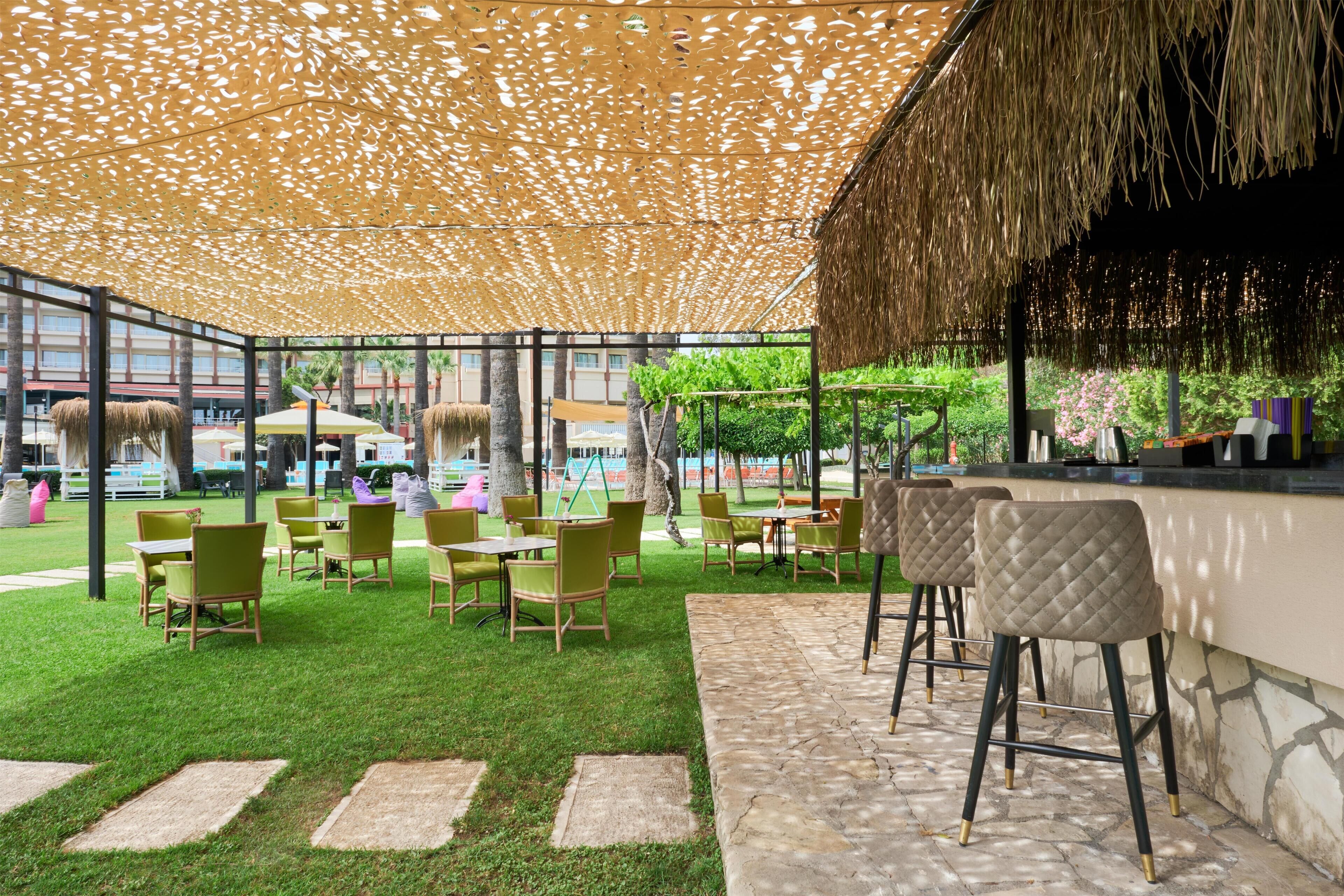 An outdoor seating area with a thatched roof, green chairs, and a bar counter.