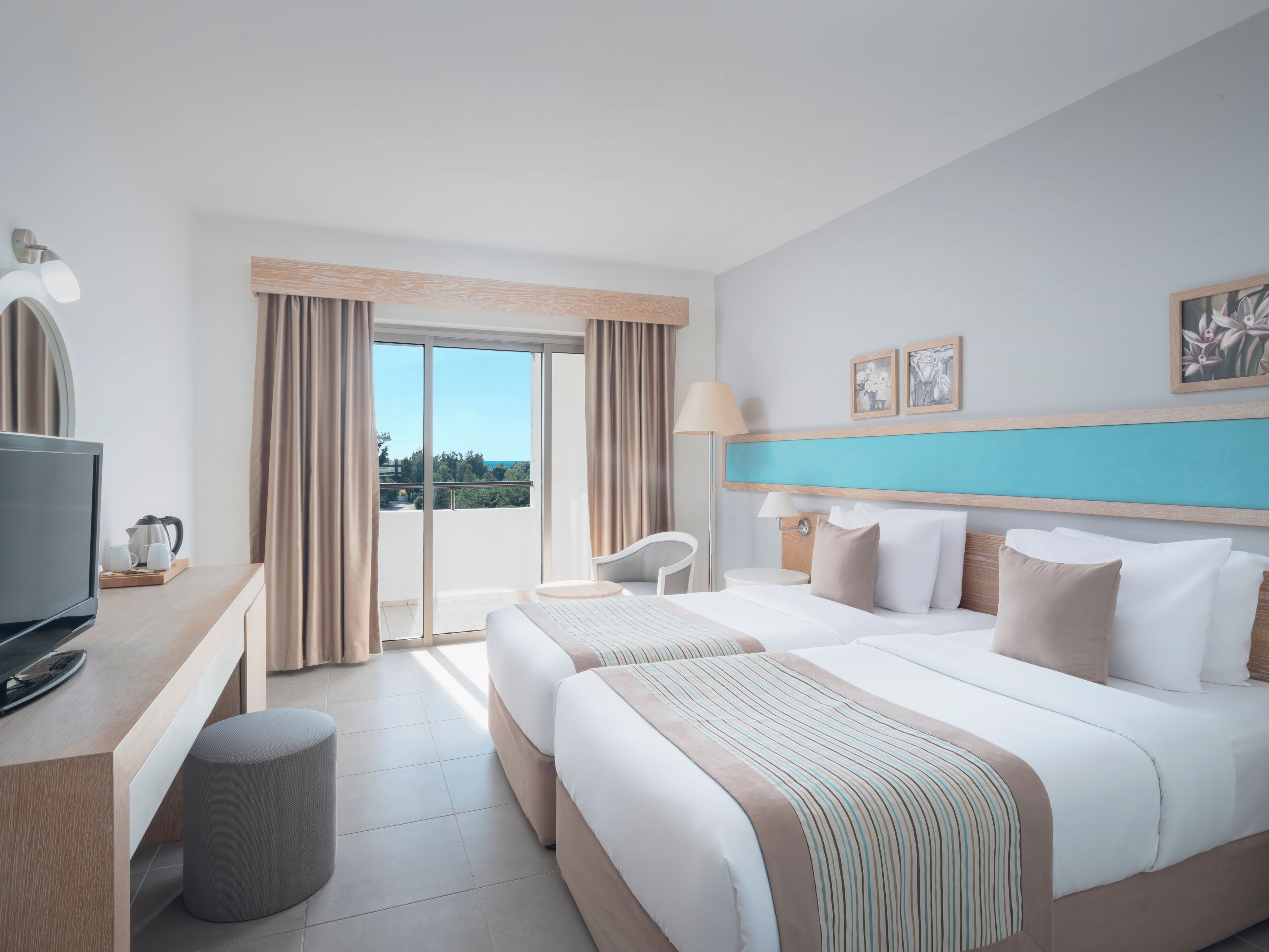 Habitación de hotel con cama, escritorio con televisor, una silla, lámpara y vistas al exterior.