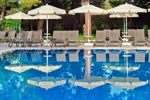 Un área de piscina con sillas de descanso y sombrillas, rodeada de árboles.