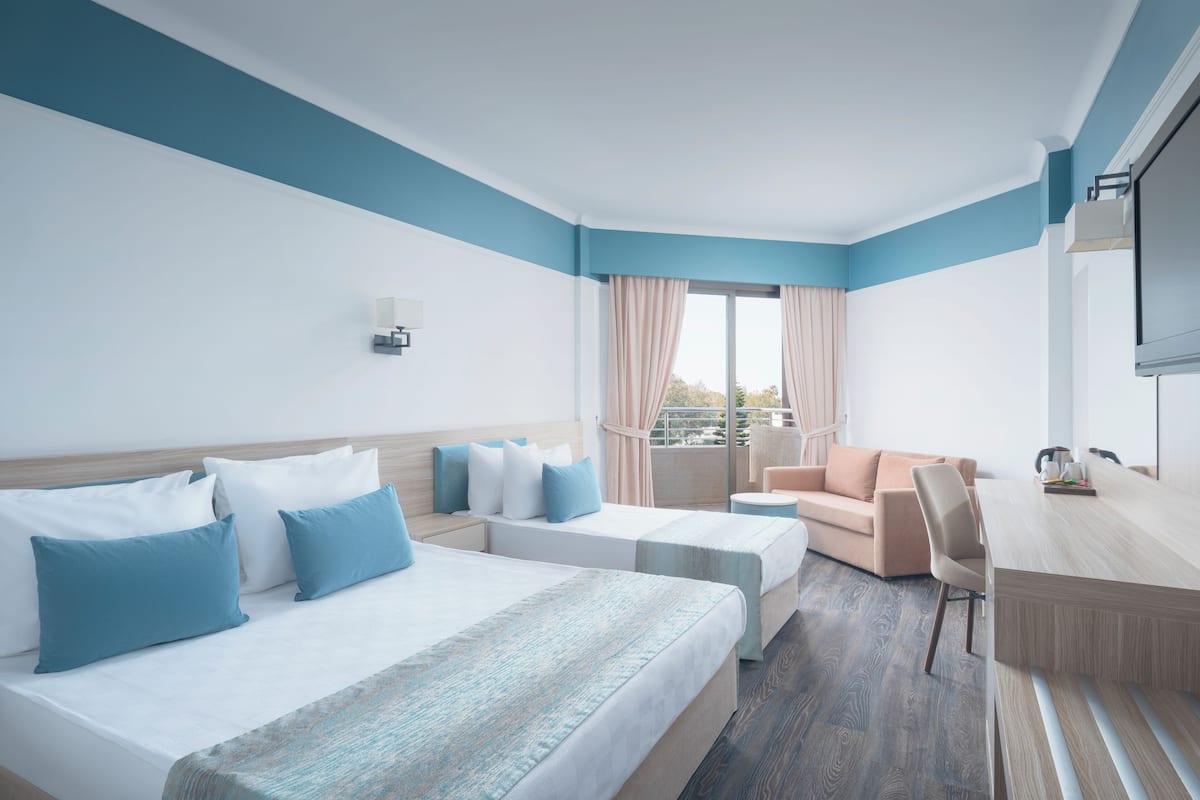 A hotel room with a large bed, a sofa, a desk, and a balcony with curtains.