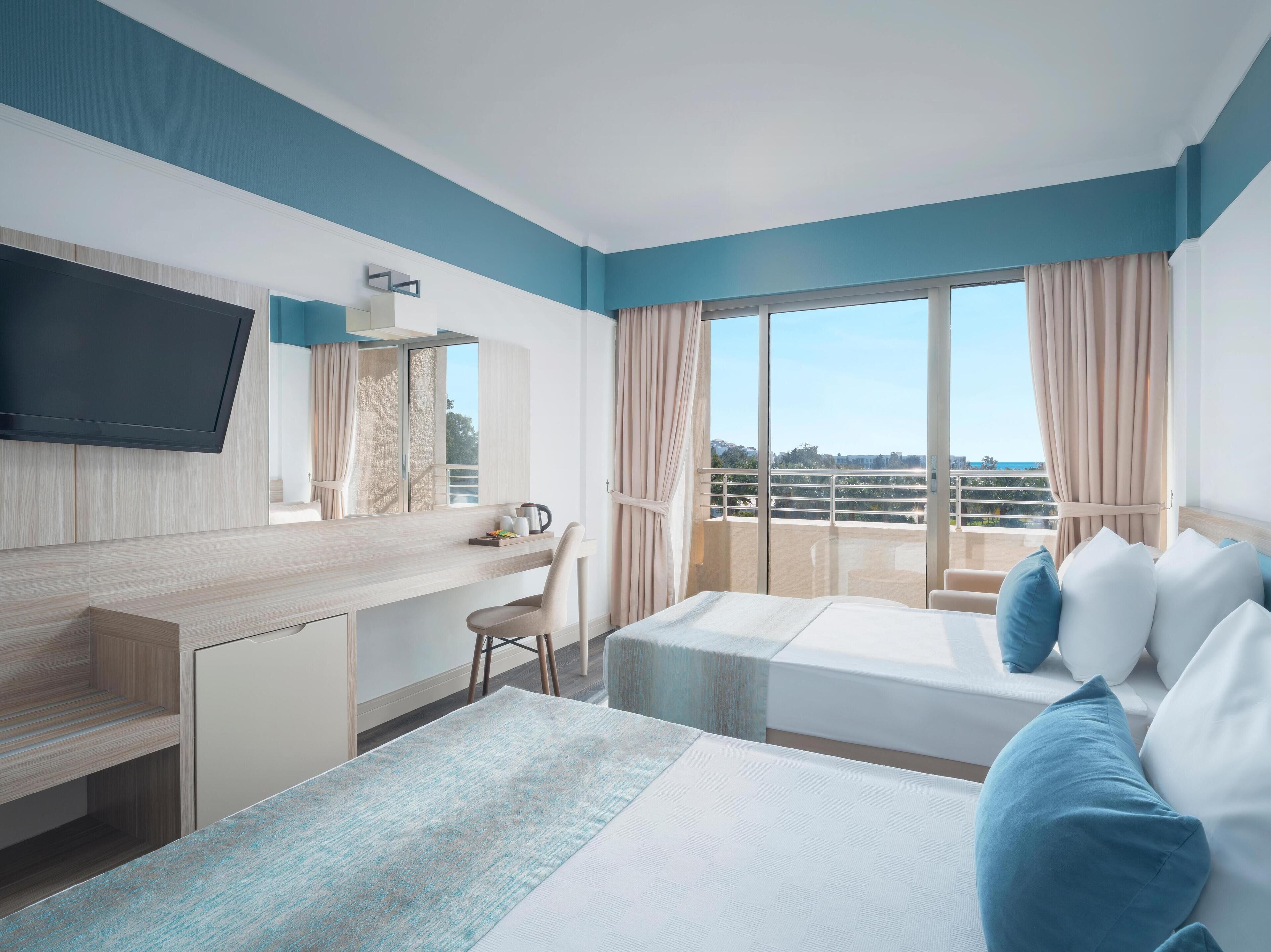 A hotel room with a bed, a desk, a chair, a TV, and a balcony with a view.